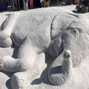 Sand sculpture of an elephant lying on its side.