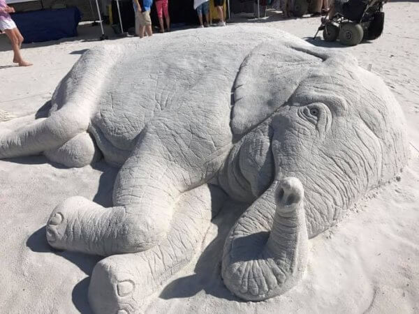 Sand sculpture of an elephant lying on its side.